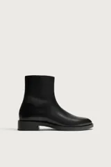 Bota de piel color negro, de caña media, con diseño liso, cierre lateral mediante cremallera, punta afilada y suela con ligero tacón.