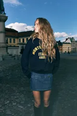 Buzo de tejido liso color azul marino, con cuello redondo y puños y bajo acanalados. Presenta un diseño bordado en amarillo en el frente con el texto "MONTE BIANCO ITALY 4805".