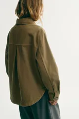 Campera camisera de sarga de algodón verde militar con cuello clásico, cierre frontal de botones y dos bolsillos delanteros de parche. Cuenta con hombros caídos, mangas largas con puños abotonados y bajo recto con aberturas laterales redondeadas.