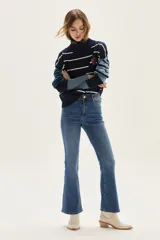 Sweater de cuello tortuga, tejido a rayas horizontales azul marino y blanco. Presenta un bordado de flor roja en el pecho y mangas largas con diseño de rayas en tonos de azul más claro.