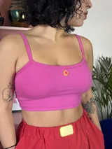 Top corto de algodón elastizado en color rosa, con breteles finos y un pequeño aplique decorativo circular en el centro del pecho.