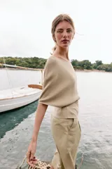 Top de punto color beige con cuello barco y mangas cortas anchas tipo murciélago. Cuenta con cintura entallada con ribete elástico y un cinturón fino de cuero sintético marrón con hebilla metálica dorada.