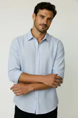 Camisa de algodón celeste claro, de corte holgado, con mangas largas, cuello camisero y cierre frontal con botones.