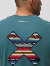 Remera de algodón orgánico color blanco, con corte regular fit y detalle de bordado en forma de X con diseño geométrico multicolor en el pecho.