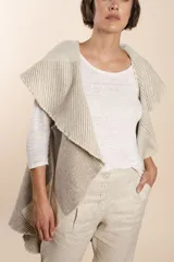 Chaleco sin mangas de tejido de lana fina sin teñir, con diseño circular y bloques de color beige y marrón. Presenta un cuello amplio y solapa que permite usarlo como chaleco largo o capa corta.