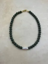 Collar artesanal compuesto por cuentas de piedra volcánica en diversos tonos y tamaños, con una perla natural de río como dije central y cierre metálico dorado.