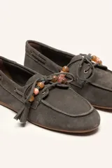 Mocasín estilo náutico de gamuza marrón, con cordones de cuero, borla decorativa y cuentas de colores en el empeine.