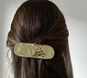 Set de accesorios compuesto por un sobre organizador de cuero gamuzado marrón con costuras decorativas, que incluye un conjunto de piezas de joyería artesanal en metal dorado: un broche, un collar de diseño geométrico con cordones de cuero, y tres pares de caravanas con diseños abstractos y orgánicos.