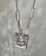 Collar de plata con cadena de eslabones alargados y dije de medalla rectangular con textura rústica, grabado en relieve con forma de estrella y una piedra brillante incrustada en el centro.