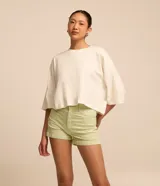 Short de sarga color blanco, de cintura alta, con bolsillos delanteros y traseros, trabillas para cinturón y bajo plegado. Cuenta con cierre frontal de botón y cremallera.