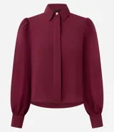 Camisa de crepé color negro, con cuello inglés, cierre frontal abotonado y mangas largas abullonadas con puños ajustados.