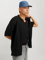 Polo de tejido estructurado negro, con hombros caídos, ajuste holgado, cuello tipo polo, mangas cortas y cierre frontal con botones.