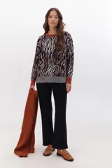 Sweater de punto con estampado animal print en tonos marrones, negros y blancos. Tiene cuello redondo, puños y bajo acanalados en color marrón y gris.
