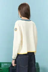 Cardigan de algodón color crudo, de corte corto y ajuste frontal con botones. Presenta detalles de ribetes a contraste en cuello, puños y ruedo, con una estética clásica y versátil.
