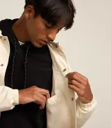 Campera color crema de poliéster con cuello inglés, abotonadura delantera con botón a presión, mangas largas con puño elástico, bajo elástico y cordón para ajustar.