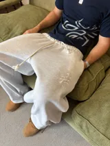 Pantalón de jogging gris melange de corte baggy, confeccionado en algodón. Presenta cintura elástica con cordón largo ajustable, bordado decorativo en la pierna izquierda y botones metálicos en la parte inferior de la botamanga para ajustar el ancho.