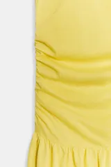 Vestido largo amarillo de algodón, con cuello barco y mangas sisa. Presenta diseño drapeado en los laterales y falda de corte evasé con volumen en el bajo.