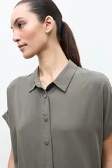 Túnica de lyocell color verde oliva, de corte holgado, con cuello camisero, cierre frontal con botones y mangas cortas con vuelta.