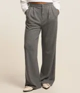 Pantalón de corte wide leg en color gris con estampado de rayas verticales finas. Presenta cintura alta con pliegues frontales, cierre de botón y cremallera, y pernera amplia.