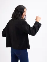 Chaqueta de gamuza sintética color negro, con cuello camisero, bolsillos frontales con solapa, cierre de botones y mangas largas.