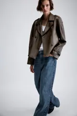 Cazadora de Zara Woman Collection confeccionada en material efecto piel color marrón oscuro. Presenta cuello con solapas, cierre frontal cruzado con botones, bolsillos delanteros y mangas largas con trabillas y hebillas ajustables en los puños.