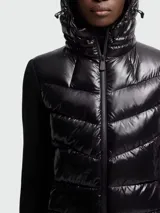 Chaqueta híbrida negra de Moncler, con cuerpo acolchado brillante y mangas de tejido de punto liso. Cuenta con capucha ajustable y cierre frontal de cremallera.