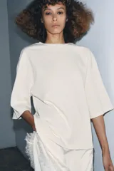 Remera color crema de algodón, corte recto, cuello redondo y mangas cortas. Presenta un panel asimétrico de encaje en el ruedo.