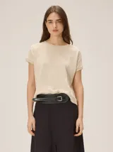 Remera tejida color beige de corte relajado, con mangas cortas y detalle de costuras frontales marcadas. Incluye un pequeño bordado distintivo en el borde inferior.