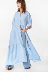 Vestido camisero largo de lino italiano color celeste, de corte relajado, con mangas caídas, jareta ajustable en la cintura, cierre frontal de botones y bajo con volado fruncido.