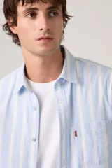 Camisa de manga larga Levi's con diseño de rayas verticales en tonos celeste y blanco. Cuenta con cuello camisero, cierre frontal de botones, un bolsillo aplicado en el pecho con etiqueta roja distintiva de la marca y dobladillo redondeado.