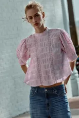 Camisa rosa de cuello alto, mangas cortas abullonadas y detalles de encaje y entredós en el frente y las mangas.
