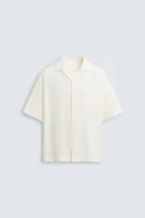 Camisa de corte relajado confeccionada en tejido de algodón con diseño jacquard floral. Presenta cuello bowling, manga corta, un bolsillo de parche en el pecho y aberturas laterales en el bajo. Cierre frontal con botones al tono.