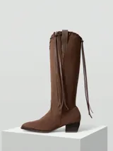Botas de caña alta confeccionadas en gamuza color marrón, con diseño de flecos laterales y taco cuadrado de altura media.