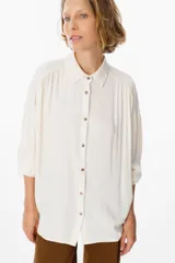 Camisa de corte oversize color chocolate, con cuello clásico, cierre frontal de botones y mangas largas con puños abotonados. Presenta un diseño fluido y holgado con sutiles frunces en los hombros.