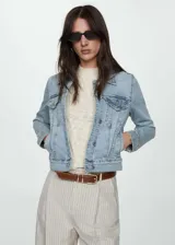 Chaqueta de jean estilo vaquero, color celeste claro, con cuello clásico, cierre frontal de botones metálicos, bolsillos con solapa en el pecho y bolsillos laterales.