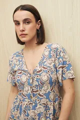 Vestido largo celeste con estampado floral en tonos beige y marrón, escote en V con botones al frente, mangas cortas y falda con leve vuelo. Confeccionado en viscosa liviana.