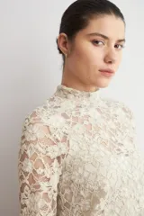 Media polera de encaje color beige, con cuello alto y mangas largas, de diseño translúcido y ajustado al cuerpo.