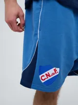Bermuda deportiva Umbro del Club Nacional de Football, modelo Nexo para hombre, en color azul marino con detalles en rojo y blanco. Cuenta con el escudo del club bordado en la pierna derecha y el logo de Umbro en la izquierda, además de cordón ajustable en la cintura.