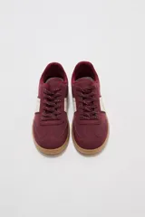 Zapatillas urbanas de color negro con suela de goma marrón, cordones negros con detalles blancos y paneles laterales.