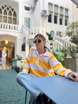 Sweater de punto a rayas horizontales amarillas y blancas, con cuello polo y mangas largas.