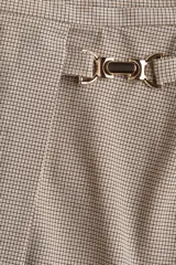 Pollera mini de corte cruzado con diseño a cuadros en tonos beige y marrón. Presenta una hebilla metálica decorativa en el lateral y cierre oculto en la parte posterior.