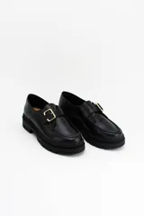 Mocasines de cuero negro con suela track y detalle de hebilla metálica dorada en el empeine.