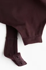 Body tanga modelador color bordó, con efecto vientre plano y sin aros. Presenta escote en V, copas forradas con fruncido central que realza el busto y tirantes finos regulables. Diseño sin costuras laterales para mayor comodidad.