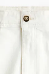 Jean de denim de algodón color blanco, de tiro alto y piernas amplias con corte holgado. Cuenta con pliegues frontales y traseros, cierre frontal con botón y bolsillos traseros de parche.