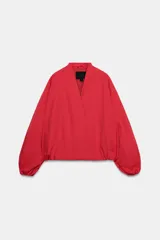 Chaqueta tipo bomber de Zara, color rojo, con escote en pico, cierre frontal cruzado con botones a presión y mangas largas abullonadas con puños elásticos. Cuenta con bolsillos delanteros y forro interior a tono.