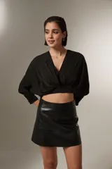 Blusa cropped de color negro, con cuello en V, mangas largas con puños ajustados y detalle de frunces en el frente.