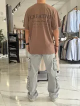 Remera oversize color beige, con diseño estampado en la espalda que incluye tipografía grande y texto descriptivo en negro.