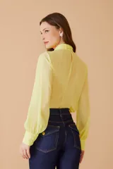 Blusa amarilla de gasa con cuello alto y lazo al cuello, mangas largas abullonadas con puños elásticos.