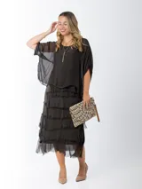 Vestido midi de seda italiana color negro, diseño dos en uno con capa superior de calce amplio, falda con volados y forro interior de algodón elastizado.