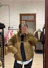 Campera puffer color tostado con cierre frontal y botones a presión. Presenta cuello alto, bolsillos laterales con cierre y diseño acolchado.